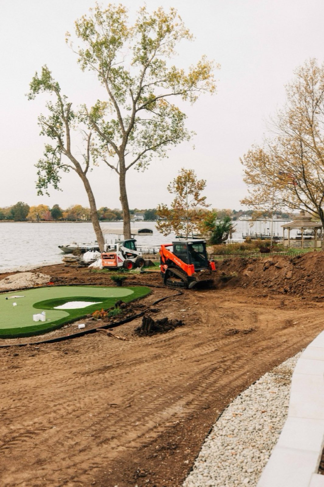 ForeverLawn Kansas City crew on-site during a lakeside putting green install — base prep with skid steers and excavator