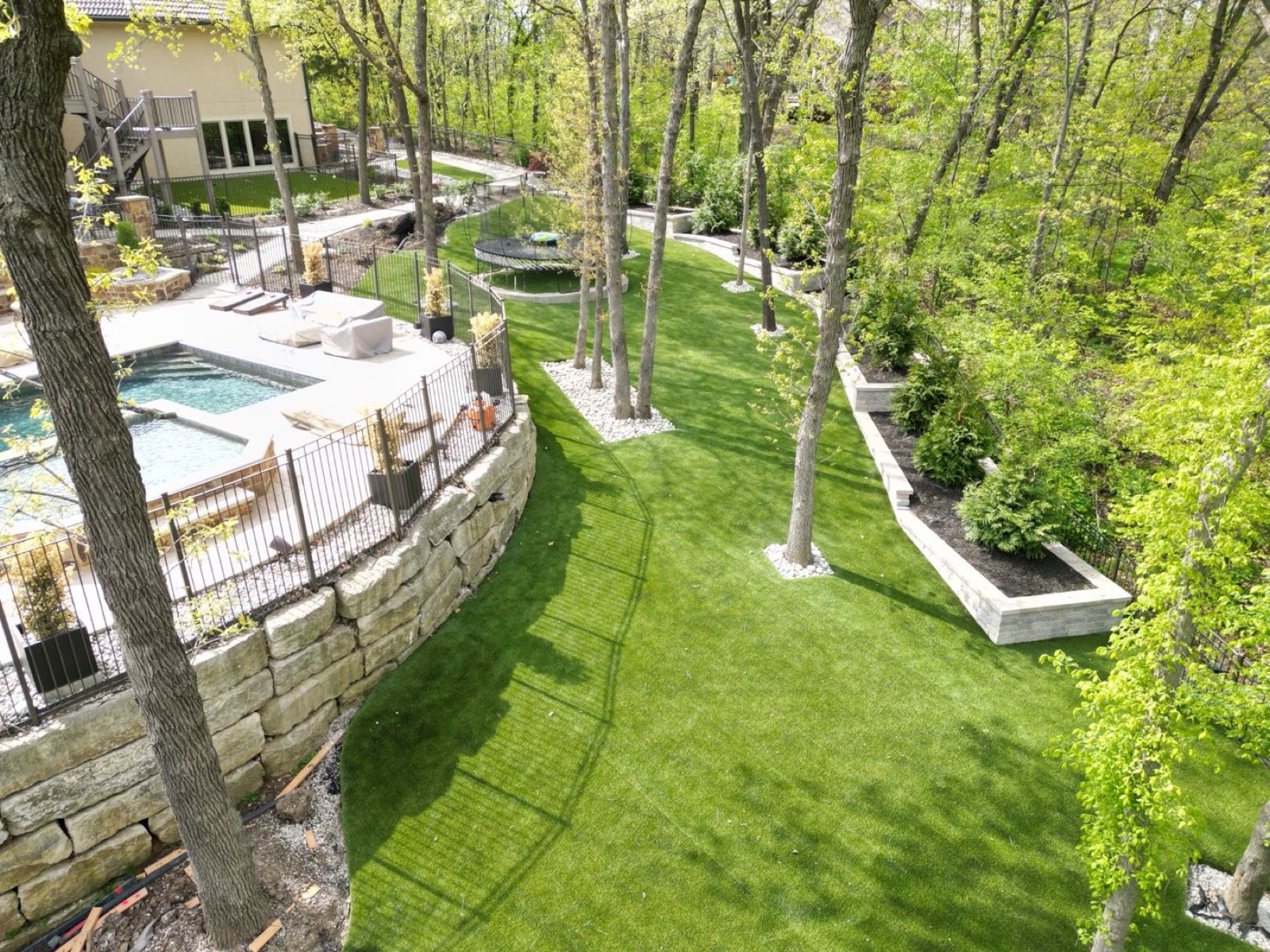 LandScapes by ForeverLawn Kansas City — drone aerial of residential install with pool, stone retaining walls, and lakeside backdrop